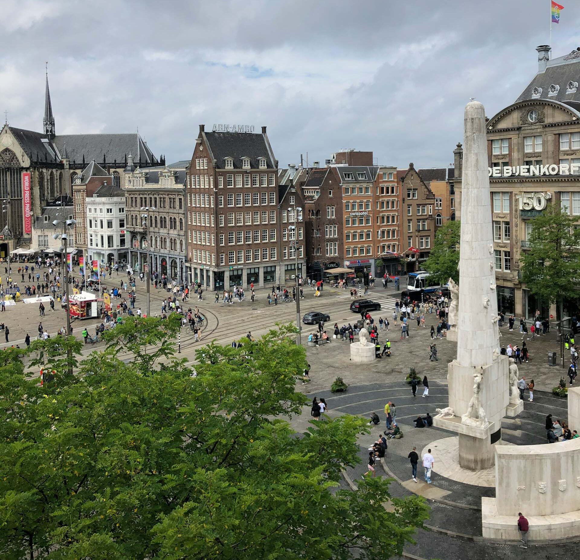 A bustling Dam Square in Amsterdam, surrounded by the Royal Palace and the National Monument, filled with people and lively activities.